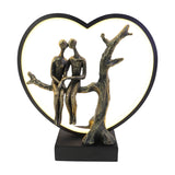 Libra Interiors Antique Bronze Couple LED lighting accessory with resin figures seated on a branch inside an illuminated black heart frame on a square base.