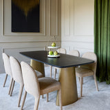 Libra Interiors black marble and brass twin-pedestal dining table styled with cream chairs, tiered centrepiece and green velvet curtain in panelled dining room.