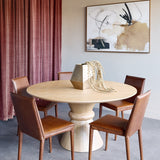 Libra Interiors Round Oak Veneer Pedestal Dining Table in natural finish, styled with brown leather chairs and a brass vase in a dining room setting.