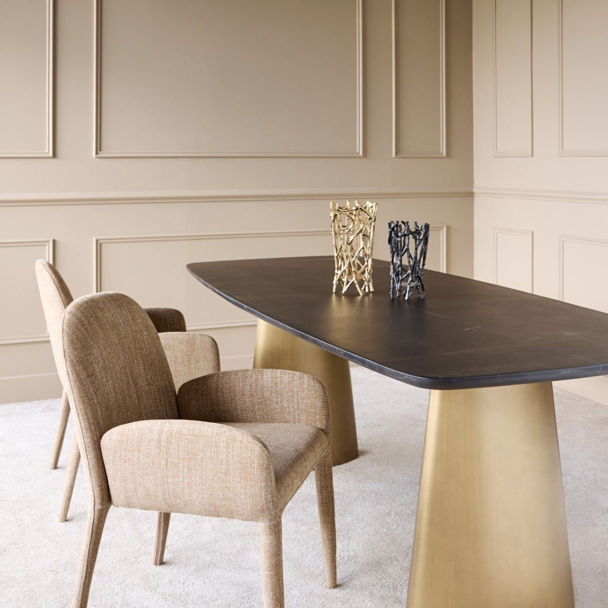 Libra Interiors wheat beige fabric carver dining chairs with rounded backs at a dark stone table on brass bases in a panelled dining room.
