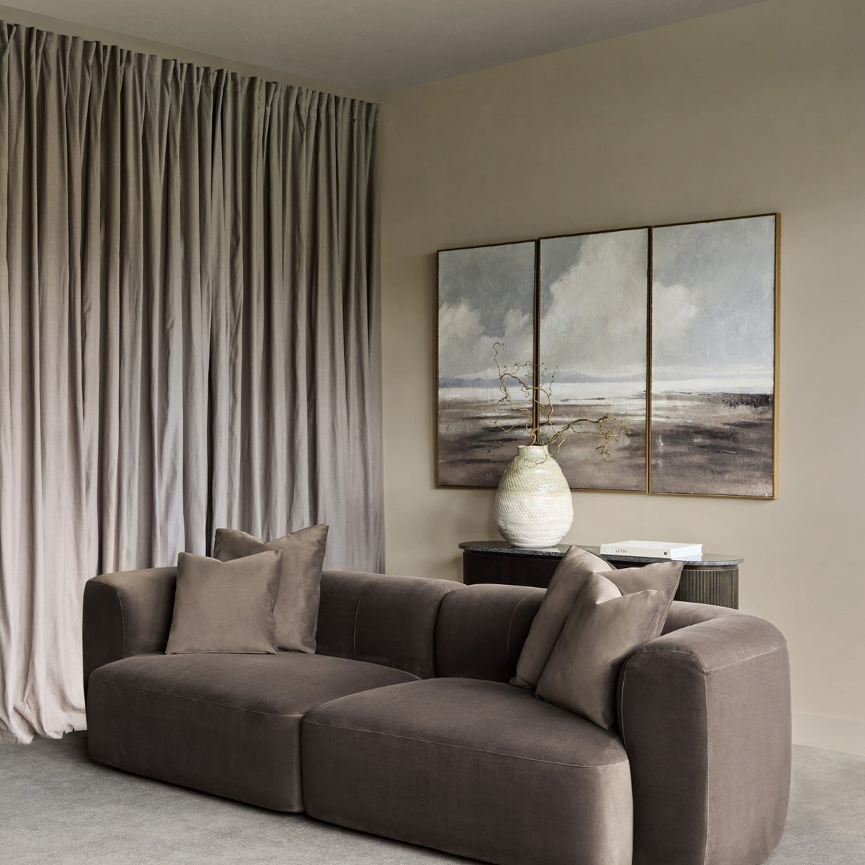 Libra Interiors brown velvet curved two-seater modular sofa with plush cushions in a neutral living room with taupe curtains and triptych wall art.