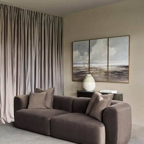 Libra Interiors brown velvet curved two-seater modular sofa with plush cushions in a neutral living room with taupe curtains and triptych wall art.