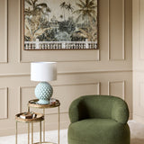 Libra Interiors Glazed Ceramic Artichoke lamp with pale green petal base and white drum shade on a brass side table beside a green bouclé armchair.