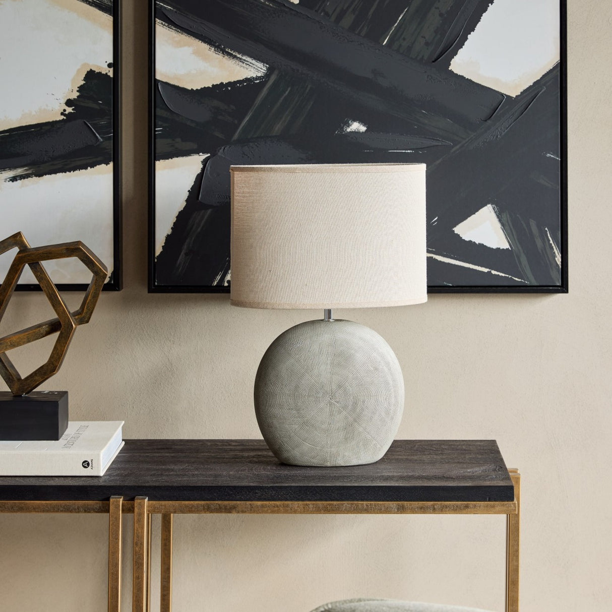 Libra Interiors Textured Ceramic Oval Table Lamp in grey with concentric ring pattern and linen-look shade, styled on a dark console beneath abstract art.