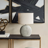 Libra Interiors Textured Ceramic Oval Table Lamp in grey with concentric ring pattern and linen-look shade, styled on a dark console beneath abstract art.