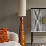 Libra Interiors Ribbed Ceramic Tapered Floor Lamp in terracotta beside a bouclé chair and striped monochrome cabinet in a neutral living room.
