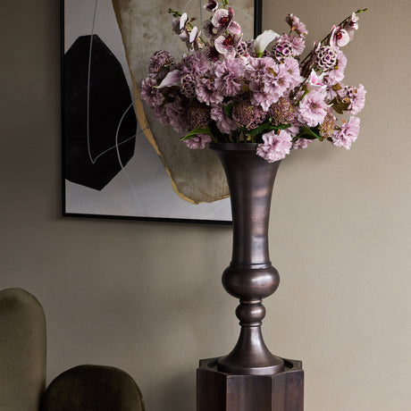 Libra Interiors Trumpet antique bronze aluminium vase with turned baluster stem, holding pink carnations and orchids beside abstract wall art in a hallway.