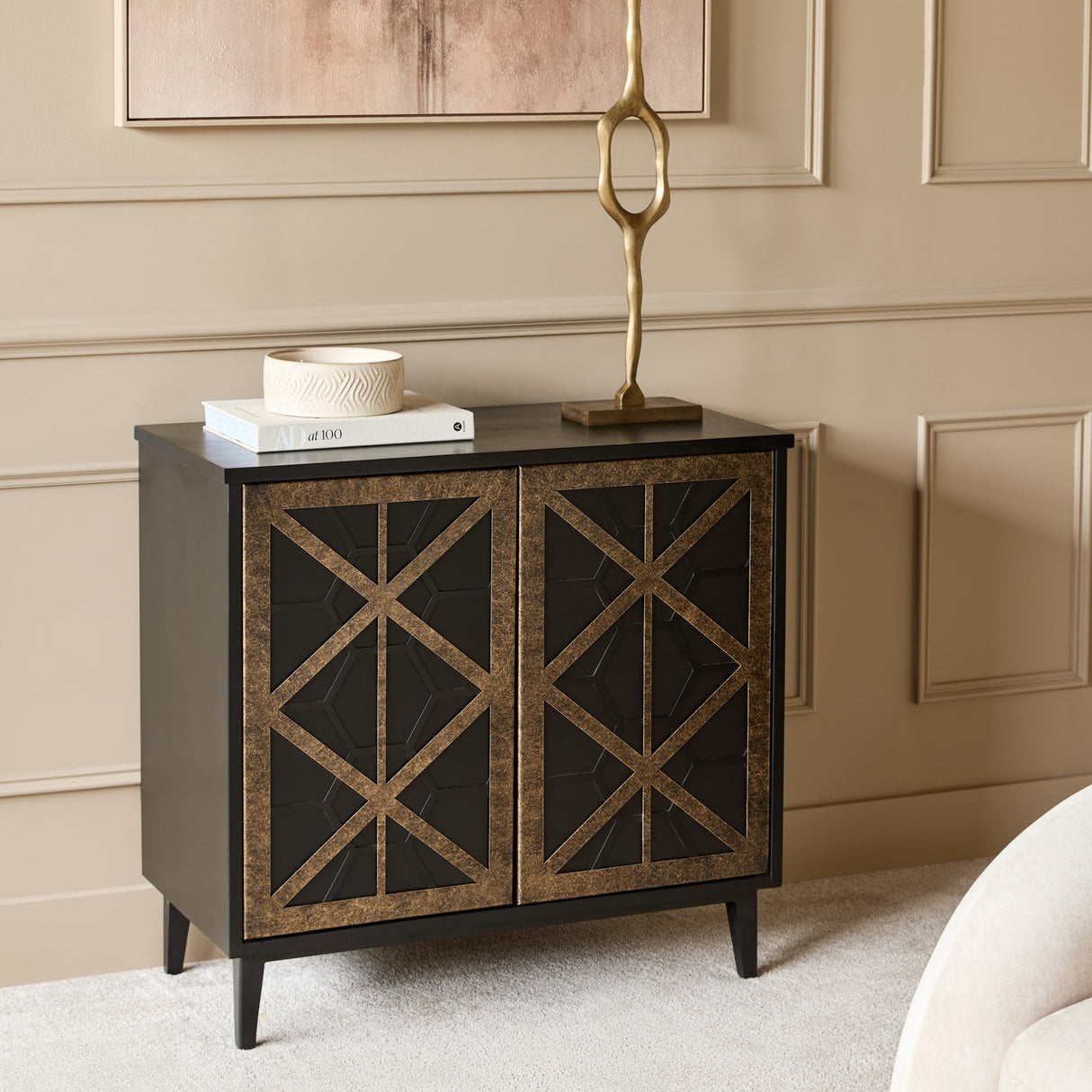 Libra Interiors Cast Aluminium Abstract Sculpture in brass, a slender rippling form on a square base, styled on a dark cabinet beside books and a bowl.