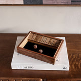 Libra Interiors Mango Wood Shut the Box game with nine numbered flip tiles and two wooden dice, displayed on an AD at 100 book atop a wooden console.
