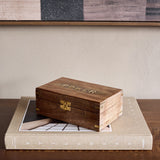 Libra Interiors Mango Wood Brass-Inlay Poker Game box with carved POKER lid and brass clasp, resting on a linen-bound book atop a dark wood console.
