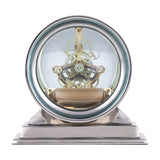 Libra Interiors Skeleton mantel clock with exposed brass cogs behind a domed glass lens, set in a round polished nickel case on a stepped base.