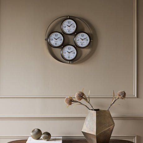 Libra Interiors Brushed Brass 4-Dial World City Wall Clock with London, New York, Hong Kong and Sydney faces, mounted on a neutral panelled wall.