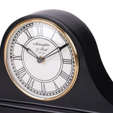 Close-up of the Libra Interiors Matt Black Roman Numeral Mantel Clock showing the white dial, black Roman numerals and antique gold bezel.