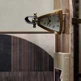 Libra Interiors Brushed Brass Curved Front Mantel Clock with rounded triangular case, white Roman numeral dial and stitched black leather handle, on a shelf.