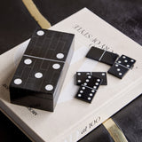 Libra Interiors Resin Inlay Black Dominoes Game shaped as an oversized domino tile with white spots, shown on a book with loose pieces beside it.