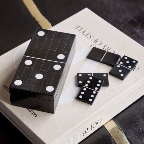 Libra Interiors Resin Inlay Black Dominoes Game shaped as an oversized domino tile with white spots, shown on a book with loose pieces beside it.