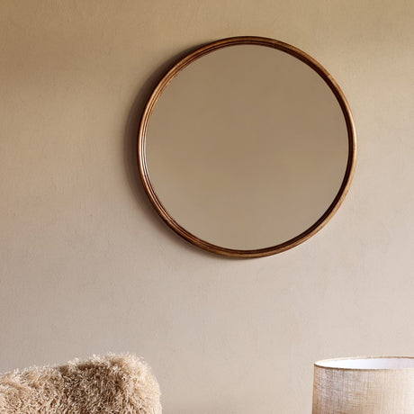 Libra Interiors Round Wood Framed Wall Mirror in light rubberwood mounted on a warm beige wall above a textured cushion and woven lamp shade.