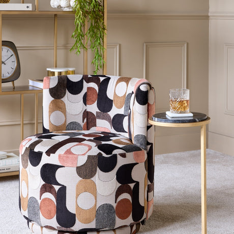 Libra Interiors round side table with black marble top and slim aged gold iron frame, styled with a whisky glass beside a patterned armchair.