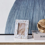 Libra Interiors Mother of Pearl Mosaic 4x6 photo frame in ivory on a marble console, styled beside a blue textured artwork, book and gold leaf decor.