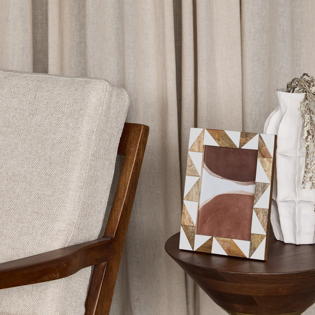 Libra Interiors Geometric Wood and Resin Photo Frame in brown with triangular inlay, displayed on a wooden side table beside a white vase and armchair.