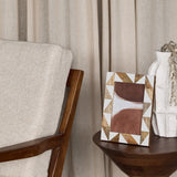 Libra Interiors Geometric Wood and Resin Photo Frame in brown with triangular inlay, displayed on a wooden side table beside a white vase and armchair.