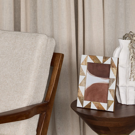 Libra Interiors Geometric Wood and Resin Photo Frame in brown with triangular inlay, displayed on a wooden side table beside a white vase and armchair.