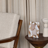 Libra Interiors Geometric Wood and Resin Photo Frame in brown and cream triangular inlay, on a walnut side table beside a ceramic vase and linen curtains.