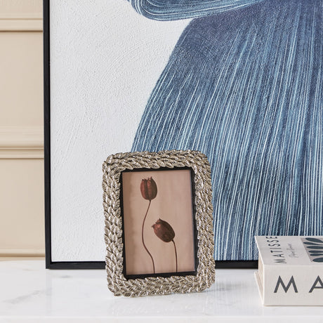 Libra Interiors Antiqued Leaf Aluminium Photo Frame in silver, displayed on a marble surface beside blue artwork and Matisse books in a living room setting.