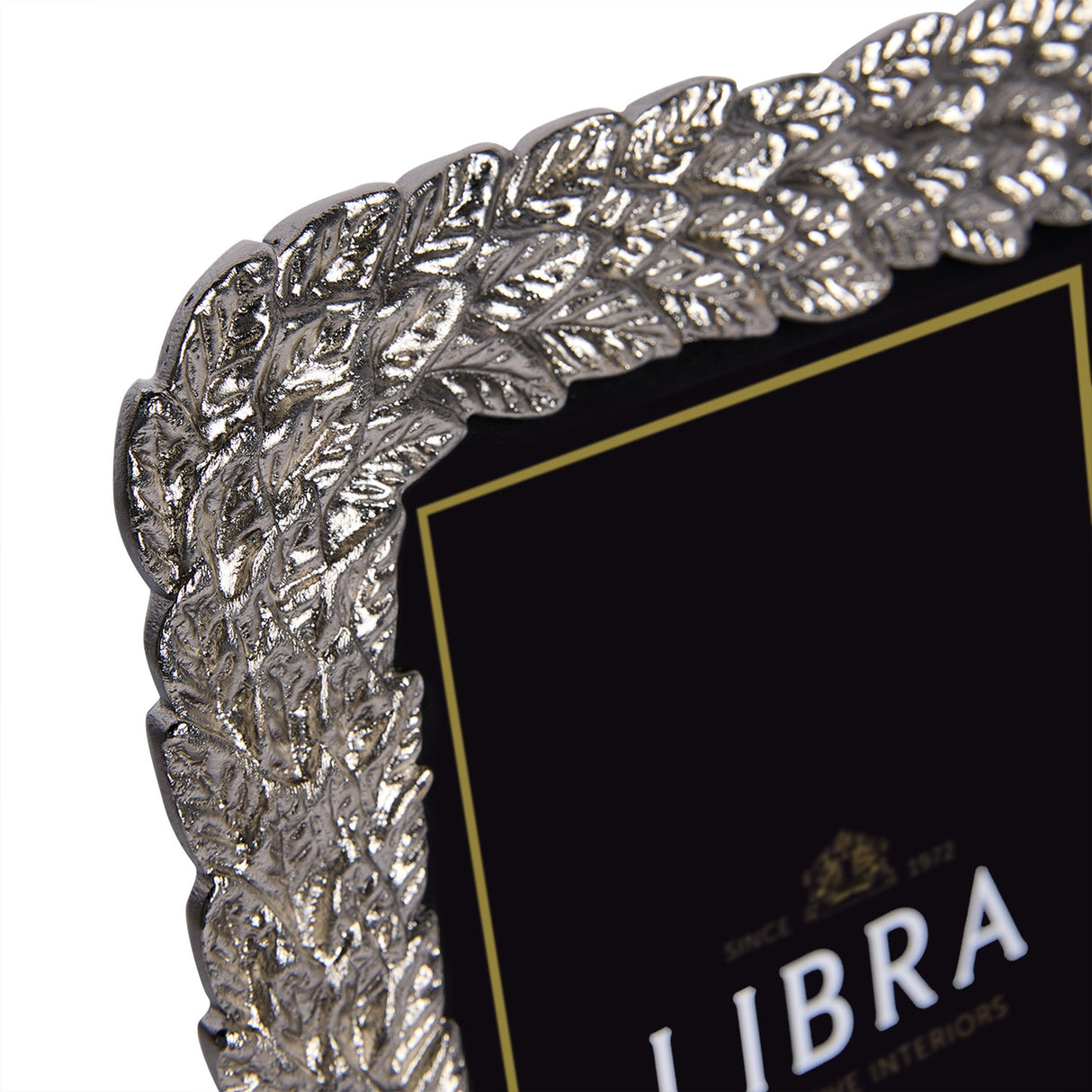 Close-up corner detail of Libra Interiors Antiqued Leaf aluminium photo frame in silver, showing raised botanical leaf motif with antiqued pewter finish.
