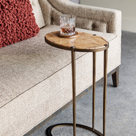 Libra Interiors Oval Marble Top side table in brown with smoked gold iron C-shaped frame, positioned beside a cream sofa holding a whisky glass.