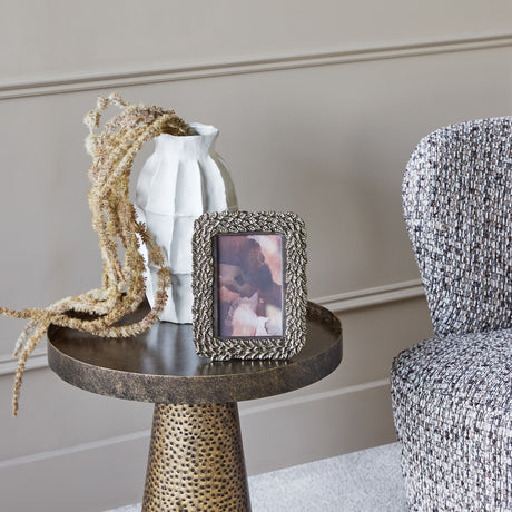 Libra Interiors Round Marble Side Table in grey with aged silver metal base, styled beside a tweed armchair with a white vase and dried grasses on top.