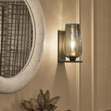 Libra Interiors Hammered Glass Tulip Wall Light in brown with tulip-shaped lustred glass shade and aged gold backplate, mounted beside a round mosaic mirror.