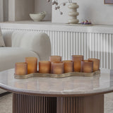 Libra Interiors Hammered Glass 9-Light Amber Lantern with staggered frosted votives on an aged gold corrugated base, on a marble coffee table.