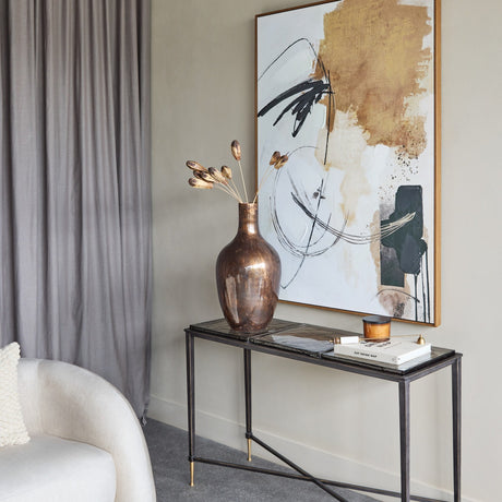 Libra Interiors Textured Glass and Iron Console Table with black tapered legs and brass tips, styled with a copper vase and abstract art in a living room.