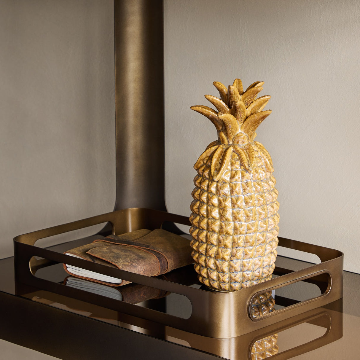 Libra Interiors Smoked Gold Glass Serving Tray in bronze holding a glazed ceramic pineapple and leather-bound notebook, styled beside a wood burner.