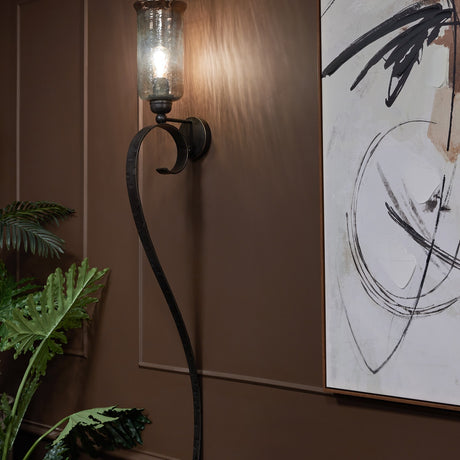 Libra Interiors Hammered Glass Iron Wall Candle Holder in brown with curved arm and lustre glass shade, mounted on a panelled wall beside abstract art.