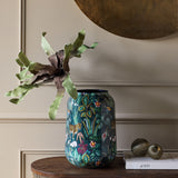Libra Interiors Enamel Iron Tropical Vase in blue with leopard and floral print, holding sculptural green leaves on a wooden console in a neutral room.
