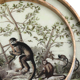 Close-up of Libra Interiors Round Glass Monkey Jungle serving tray in gold, showing the printed monkeys among leafy branches behind glass with antiqued frame.