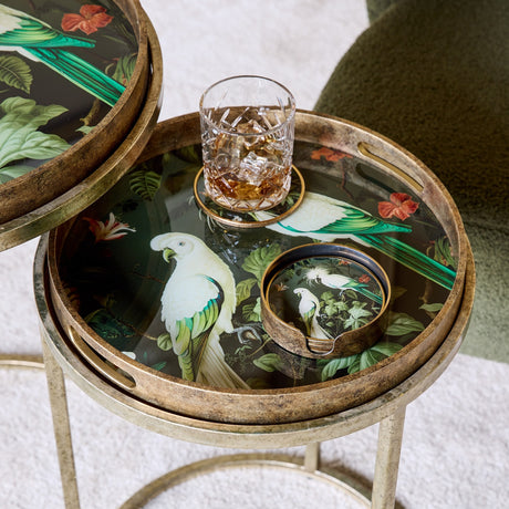 Libra Interiors Tropical Bird round acrylic coasters in antique gold holder, styled on a bird-print tray table beside a whisky glass.
