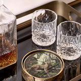 Libra Interiors Jungle Print round acrylic coaster with leopard illustration and antiqued gold rim, styled on a bar tray beside crystal glasses and a decanter.