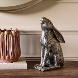 Libra Interiors Antique Bronze Stargazing Hare Sculpture in textured resin, sitting on a wooden console beside a pink ceramic vase and book below a mirror.
