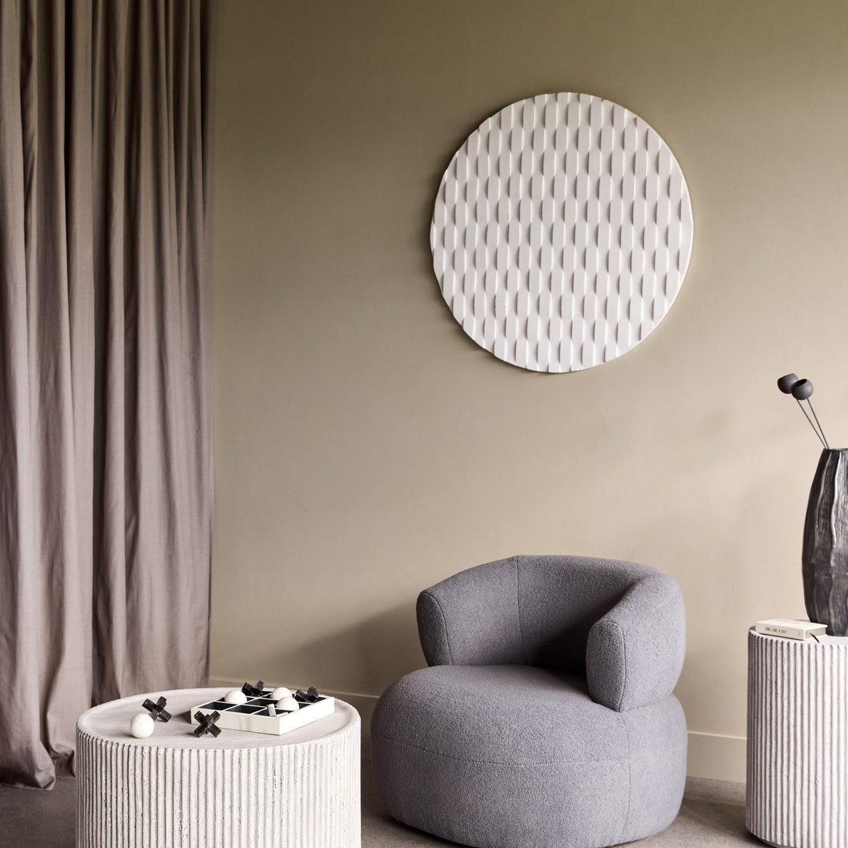 Libra Interiors Fluted Round Coffee Table in grey with ribbed stone effect finish, styled beside a grey bouclé armchair in a neutral living room.