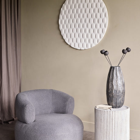 Libra Interiors ribbed stone effect cylindrical side table in grey, styled with a textured glass vase beside a grey bouclé armchair and round wall art.