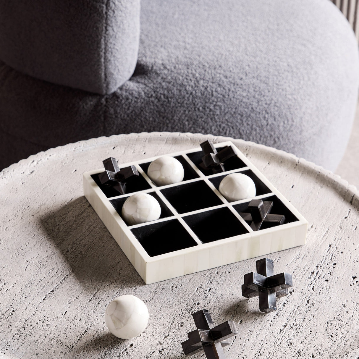 Libra Interiors bone and horn inlay noughts and crosses game with white bone balls and black horn crosses, displayed on a pale round coffee table.
