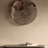 Libra Interiors Coral Openwork Round Wall Art in bronze, a large aluminium coral-inspired latticework disc mounted above a marble console with books.