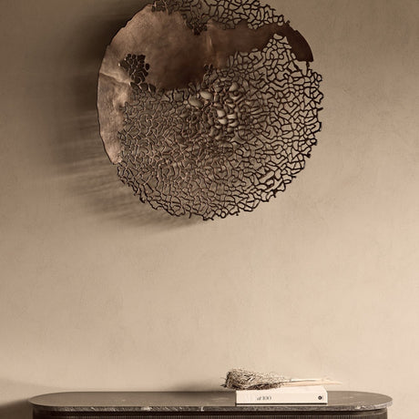 Libra Interiors Coral Openwork Round Wall Art in bronze, a large aluminium coral-inspired latticework disc mounted above a marble console with books.
