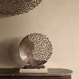 Libra Interiors Coral Cut-Out round aluminium sculpture in bronze on a black base, displayed on books atop a marble sideboard with matching wall art above.