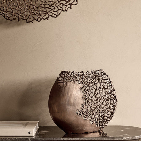 Libra Interiors Coral Cut-Out Aluminium Ellipse Vase in bronze on a marble console, with coral-inspired lattice detailing beside a book against a neutral wall.