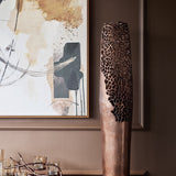 Libra Interiors Coral Cut-Out raw bronze floor vase with pierced coral lattice upper and smooth base, beside abstract framed art in a warm-toned interior.