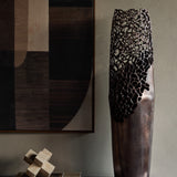 Libra Interiors Coral Cut-Out bronze aluminium floor vase with smooth base and pierced openwork top, styled beside abstract art and a travertine sculpture.